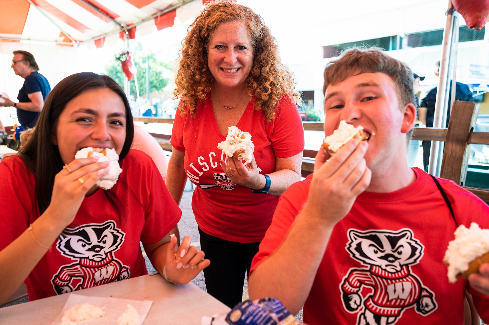 Two Badger Ambassadors Eating Puff Pastries at the Wisconsin State Fair with UW-Madison Chancellor Jennifer L. Mnookin
